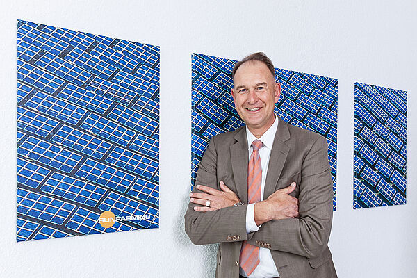 Herr Schrumm im Anzug vor Fotos mit Solarpaneln